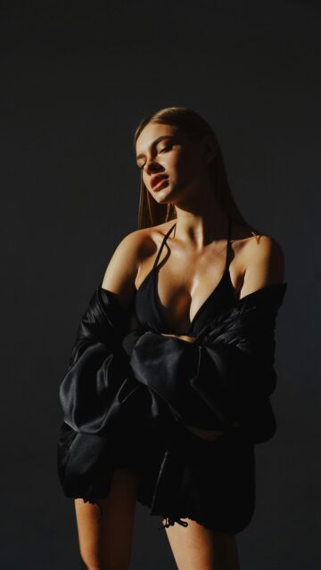 Portrait of a woman posing with crossed arms in a shadowy studio setting, exuding elegance.