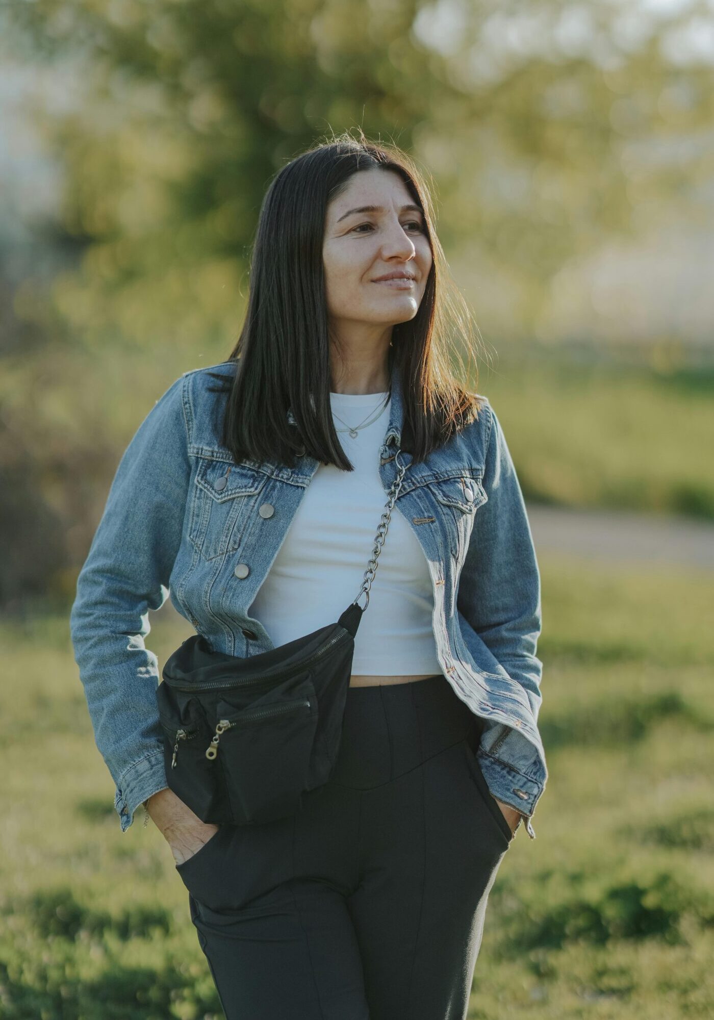 A woman in a denim jacket enjoys a sunny day outdoors in a natural setting.