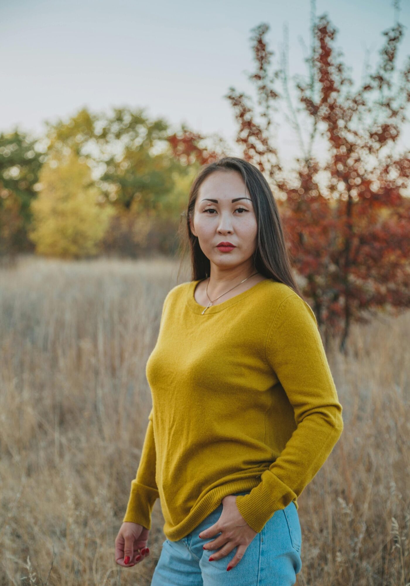 Charismatic ethnic female standing in countryside and holding hand in pocket while looking at camera